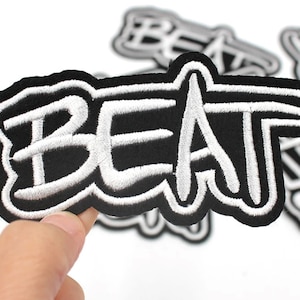May include: Black and white embroidered iron-on patch with the word "BEAT" in a stylized font.