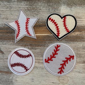 May include: Four baseball-themed patches. A white star-shaped patch with red stitching, a heart-shaped patch with a baseball design, a baseball-shaped patch, and a gray circular patch with red stitching.