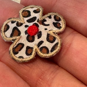 May include: A brown and white leopard print fabric flower with a red center. The flower is sewn with a gold thread around the edges.