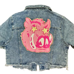 May include: A blue denim jacket with short sleeves and a pink pig with gold glitter stars for eyes on the back.