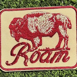 May include: A beige embroidered patch with a red buffalo silhouette and the word "Roam" in red lettering.