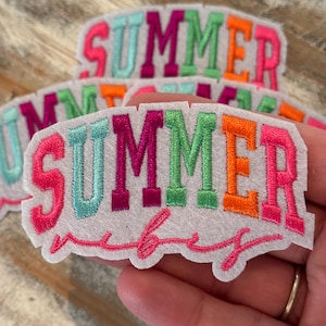 May include: White felt patches embroidered with the word "SUMMER" in various colors, including pink, teal, orange, and green. The word "vibes" is embroidered in pink script below the word "SUMMER".