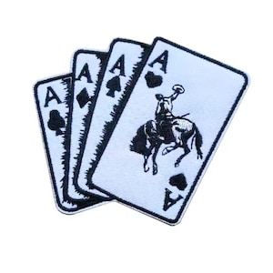 May include: Embroidered patch featuring four playing cards, all aces. The cards are white with black detailing, including suits and a cowboy riding a horse. The patch has a black border.
