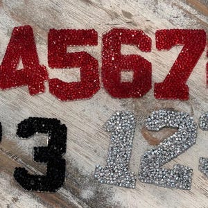 May include: Red, black, and silver glitter numbers 1 through 9 and 123. The numbers are in a bold, block font.