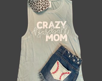 May include: A light blue sleeveless shirt with the text "CRAZY Baseball MOM" in white. The shirt is paired with denim shorts that have a baseball stitched on the back pocket.