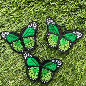 May include: Three green embroidered butterfly patches with black outlines and white accents.