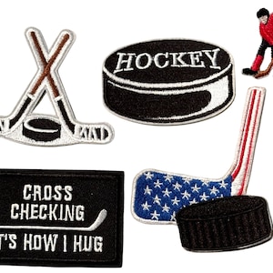 May include: Set of five embroidered iron-on patches featuring hockey-themed designs. The patches include a hockey puck with crossed sticks, a hockey puck with the word "HOCKEY" on it, a hockey stick with an American flag design, a hockey stick with a puck, and a black patch with white text that reads "CROSS CHECKING IT'S HOW I HUG".