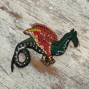 May include: Green and red embroidered dragon patch with a yellow and white wing. The dragon is curled up with its tail in its mouth.