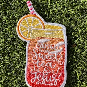 May include: A red, orange, and yellow embroidered patch of a mason jar with a straw and a lemon slice. The text on the patch reads "Raised on Sweet Tea & Jesus".