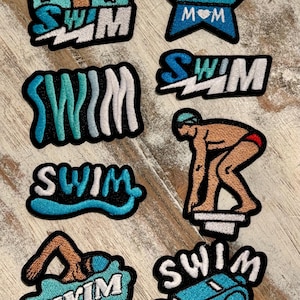 May include: A collection of embroidered patches with a swimming theme. Designs include the word "SWIM" in various fonts and styles, a star-shaped patch with "SWIM MOM", and illustrations of swimmers and a coach's whistle.