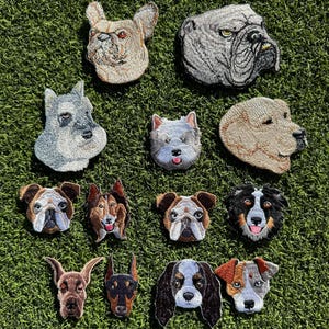May include: A collection of 12 embroidered iron-on patches featuring different dog breeds. The patches are in various colors and designs, including a bulldog, a schnauzer, a french bulldog, a labrador, a border collie, a doberman, a cocker spaniel, and a westie.