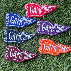 May include: Six embroidered iron-on patches in different colors, each featuring a white pennant with the text "GAME DAY" in a script font.