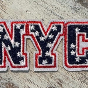 Pu&ograve; includere: Una toppa ricamata in rosso, bianco e blu con le lettere NYC. Le lettere sono contornate di bianco e rosso, e lo sfondo &egrave; un motivo di stelle blu e bianche.