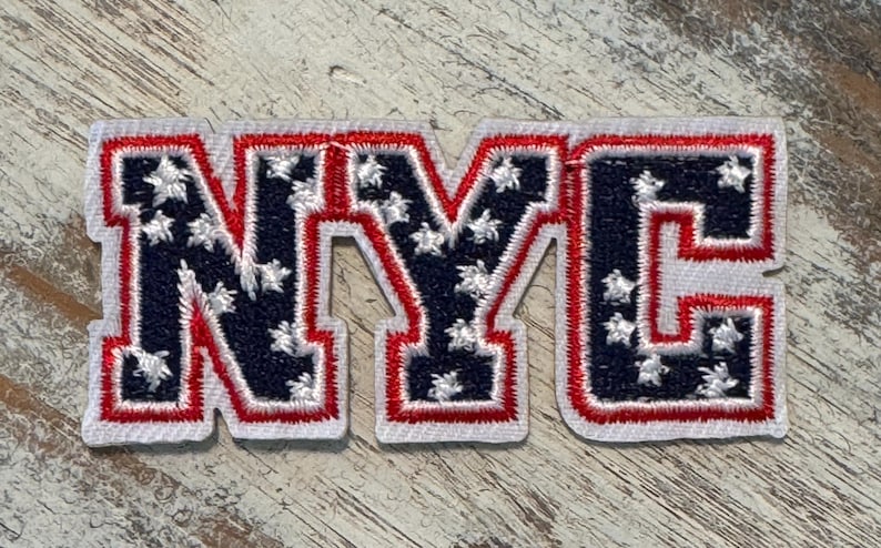 Pu&ograve; includere: Una toppa ricamata in rosso, bianco e blu con le lettere NYC. Le lettere sono contornate di bianco e rosso, e lo sfondo &egrave; un motivo di stelle blu e bianche.