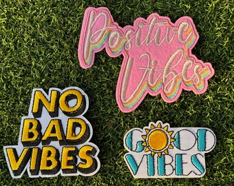 May include: Three embroidered iron-on patches with positive messages. The patches are white with black and yellow lettering. The first patch says "No Bad Vibes". The second patch says "Positive Vibes" in pink with rainbow accents. The third patch says "Good Vibes" in blue with a yellow sun graphic.