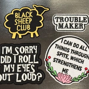 May include: Four embroidered iron-on patches with different sayings. The first patch is black with yellow stitching and says "Black Sheep Club". The second patch is white with black stitching and says "Trouble Maker". The third patch is black with white stitching and says "I'm Sorry Did I Roll My Eyes Out Loud?". The fourth patch is white with black, green, pink, and red stitching and says "I Can Do All Things Through Spite, Which Strengthens Me".