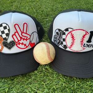 May include: Two black and white trucker hats with various patches, including a peace sign, baseballs, hearts, and checkered patterns. The text "I Love Umpires" is on one hat.