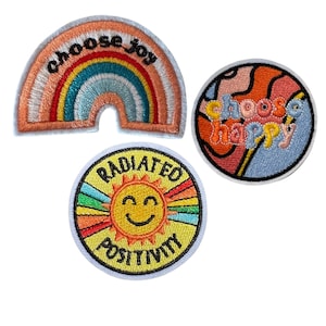 May include: Three embroidered iron-on patches with positive messages. The first patch is a rainbow with the text "choose joy". The second patch is a swirl design with the text "choose happy". The third patch is a yellow sun with the text "radiated positivity".