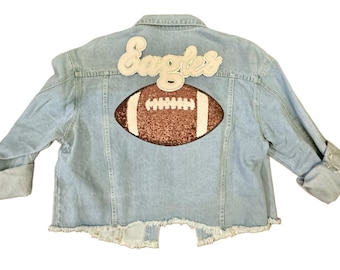 May include: Light blue denim jacket with a white "Eagles" patch and a brown sequined football patch on the back.