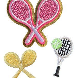 May include: Embroidered patches featuring tennis-themed designs. The patches include crossed pink tennis rackets on a gold glitter background, crossed yellow rackets, and a single racket with a tennis ball.