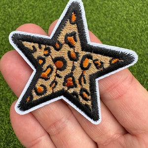 May include: A brown and black star-shaped patch with a leopard print design. The patch has a white border.