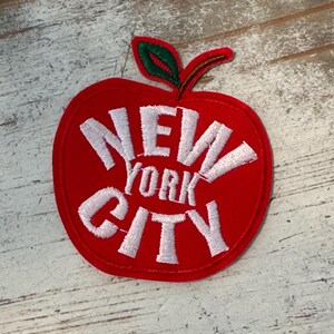 Pu&ograve; includere: Toppa a forma di mela rossa con testo ricamato bianco che recita "NEW YORK CITY".