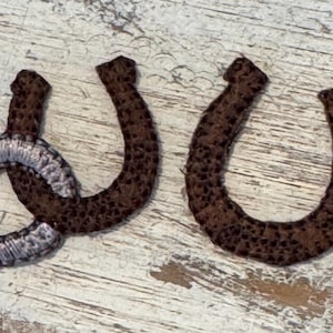 May include: Two brown leather horseshoes with a silver horseshoe in the middle.