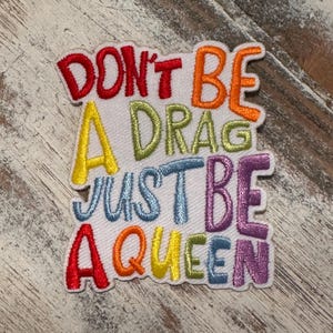 May include: A colorful embroidered patch with the text "Don't be a drag, just be a queen".