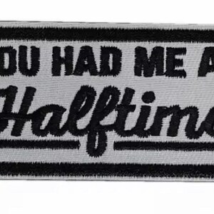 May include: A rectangular patch with the phrase "YOU HAD ME AT Halftime" embroidered in black on a light gray background. The patch has a black border and is likely designed to be sewn onto clothing or accessories.