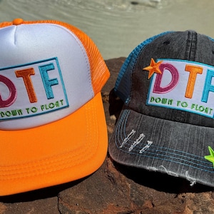 May include: Two trucker hats with the text "DTF DOWN TO FLOAT". One hat is orange and white, the other is gray and blue. Both hats have a mesh back and a curved brim. The gray hat has star accents.