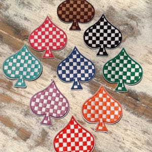 May include: Nine embroidered iron-on patches in the shape of a spade with a checkered pattern. The patches are in various colors including red, orange, green, blue, purple, brown, and black.