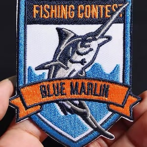 May include: A blue and orange embroidered patch with a marlin fish and the text "Fishing Contest Blue Marlin".
