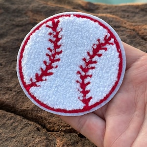 May include: White and red embroidered baseball patch. The patch is round and has a white background with red stitching. The stitching forms the shape of a baseball.