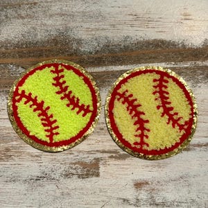 May include: Two yellow and red softball patches with gold glitter trim. The patches are made of fuzzy fabric.