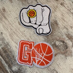 May include: Two embroidered patches with a basketball theme. One patch features a white fist holding a basketball. The other patch has the word "GO" in orange and a basketball.