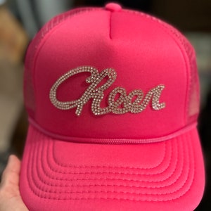 May include: Pink trucker hat with a mesh back and a rhinestone "Queen" design.