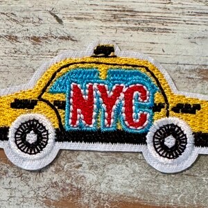 Pu&ograve; includere: Toppa ricamata gialla di un taxi di New York City con la parola "NYC" in lettere rosse sul lato.