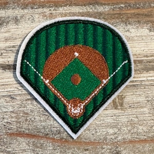 May include: Embroidered baseball field patch featuring a green outfield with brown infield and white stitching for the base lines. The patch has a white border and is designed to be sewn onto clothing or accessories.