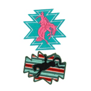 May include: Two embroidered patches featuring rodeo themes. One patch has a pink rider on a bucking bronco within a turquoise geometric shape. The other patch shows a black rider on a bucking bronco with a striped background.