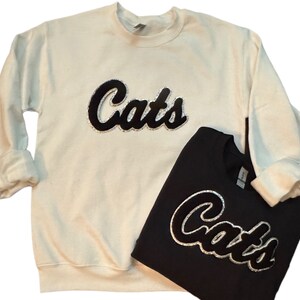 May include: Two sweatshirts, one white and one black, with the word "Cats" in a sparkly black script on the front.