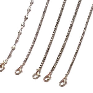 May include: Five different silver chains with lobster clasps. The chains are all different styles, including a heart-shaped chain, a box chain, a curb chain, and a rope chain.