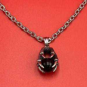 May include: A silver chain necklace with a pendant featuring a black gemstone held in a silver claw design.