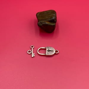 May include: A silver-toned padlock and key charm with a keyhole design. The padlock is closed and the key is separate.