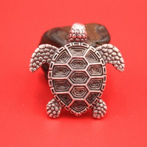 May include: A silver turtle pendant with a detailed shell design. The pendant is a popular choice for jewelry making and is a symbol of good luck and longevity.