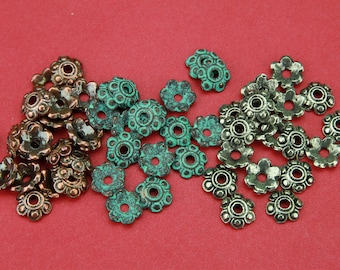 Könnte beinhalten: Eine Sammlung antiker Metallperlen in Blumenform in Kupfer- und Grüntönen. Die Perlen haben eine patinierte Oberfläche und sind perfekt für die Schmuckherstellung oder zum Basteln.
