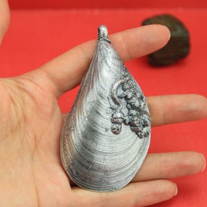 May include: A silver pendant shaped like a clam shell with a detailed design of a cluster of grapes on the surface.