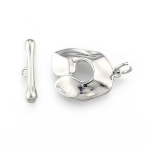 May include: Silver tone toggle clasp with a smooth, rounded bar and a textured, abstract, heart-shaped piece.