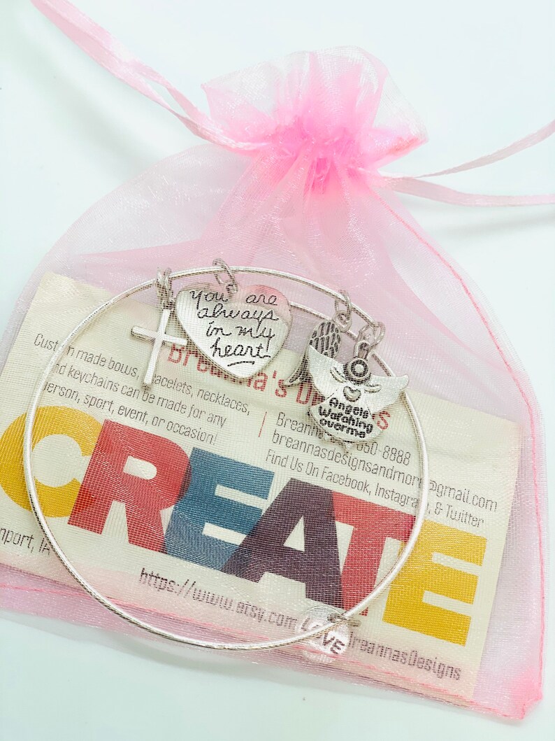 Peut inclure: Un bracelet &agrave; breloques argent&eacute; avec un charme en forme de c&oelig;ur qui dit "You are always in my heart!" et un charme d'ange qui dit "Angel watching over me". Le bracelet est dans un sac en organza rose avec une carte qui dit "Brea's Angels" et une adresse de site web.