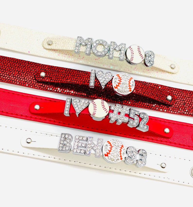 May include: Four white and red leather bracelets with rhinestones and baseball charms. The bracelets feature the words "MOM", "I LOVE", "#52", and "BEN#93".