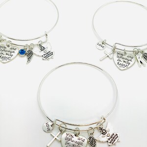 Peut inclure: Trois bracelets en argent avec des breloques, dont un c&oelig;ur avec le texte "you are always in my heart", une croix, une aile et un petit charme rond avec le mot "LOVE".